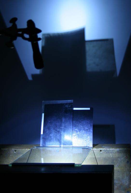 Side view of the same setup showing the glass plate between blocks, two polarizing filters standing behind it, and the flashlight on the ring stand above casting light down onto the glass