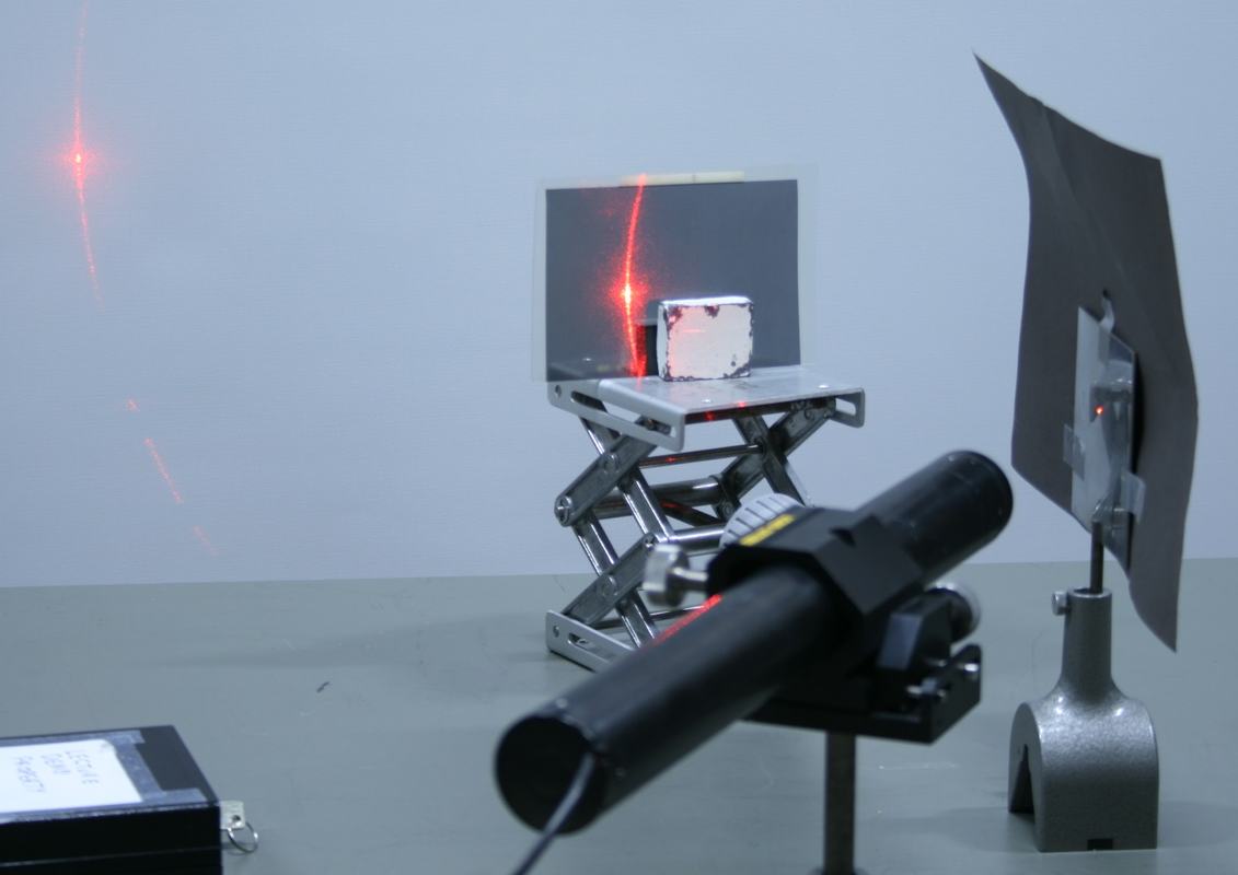Close-up of steel plate showing bright red laser reflection and scatter on plate surface, wall, and through analyzer