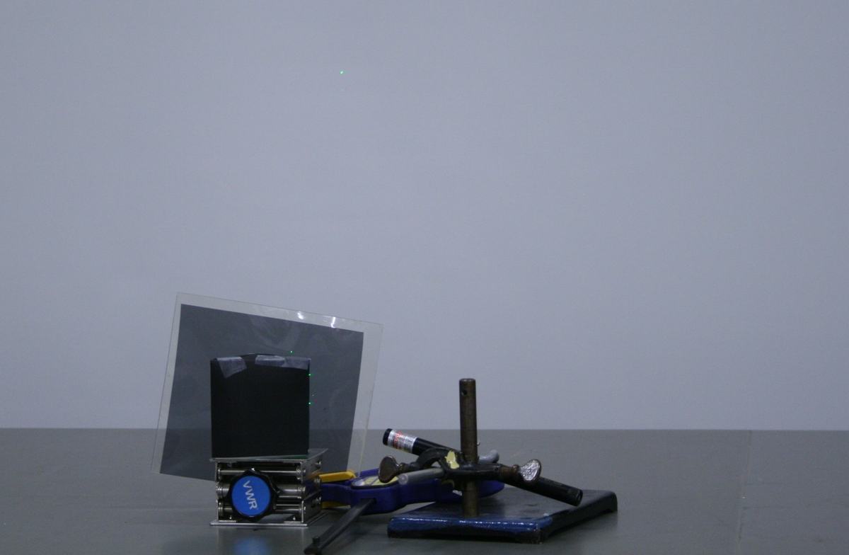 Slightly different angle of the same Brewster's angle setup, with a single green laser dot visible on the wall — the reflected beam is nearly extinguished