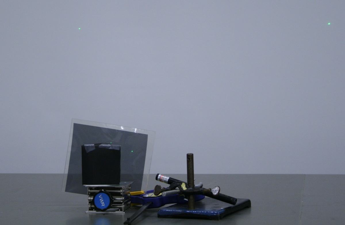 Same apparatus from a wider angle showing both the reflected and refracted green laser dots separated on the wall