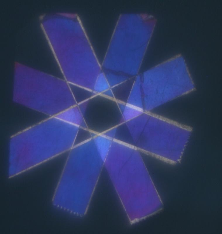 Overlapping cellophane tape strips arranged in an asterisk pattern between crossed polarizers, showing blue and purple colors where strips overlap