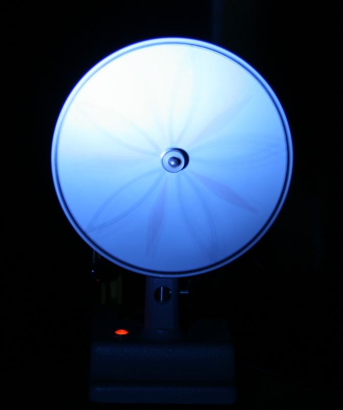 Spinning disk under blue strobe showing many radial lines blurred into a dense spoke pattern with slight motion blur