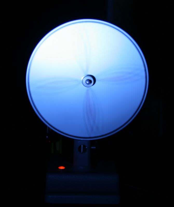 Spinning disk under blue strobe showing radial lines blurred into a smooth continuous appearance with faint spoke shadows