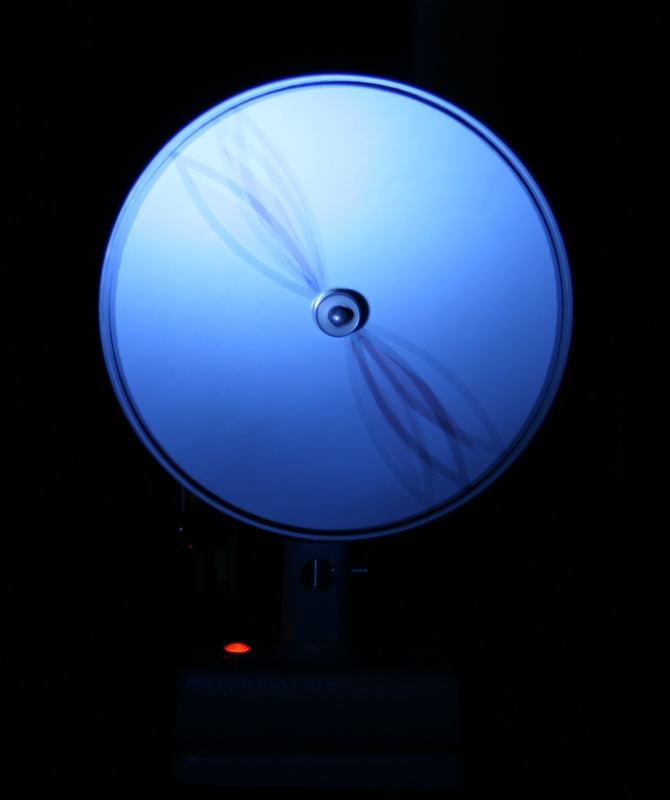 Spinning disk under blue strobe showing a radial spoke pattern with visible motion blur; red power indicator light at base of rotator