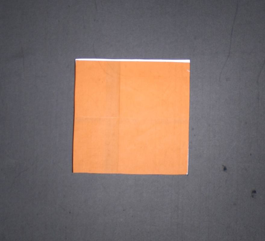 Orange origami paper square with fold creases on dark background, appearing bright and saturated