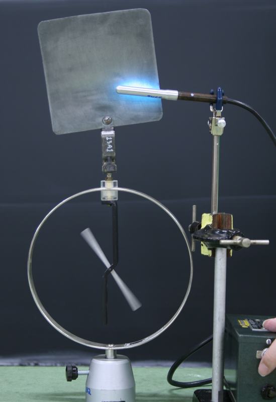 Projection electroscope with zinc plate clipped to the top knob and a quartz-encased mercury lamp glowing blue, mounted on a ring stand with finger clamp and aimed at the plate
