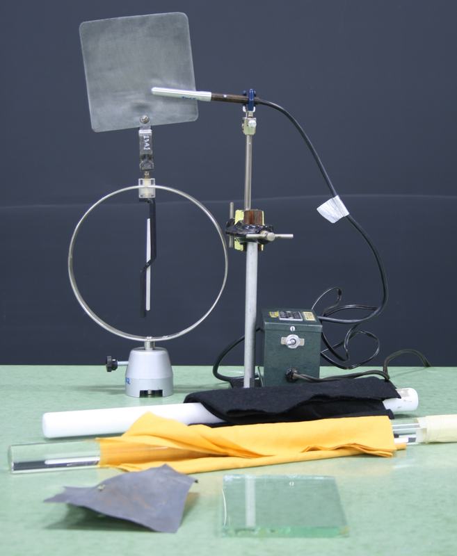 Full equipment layout on green table: projection electroscope with zinc plate, mercury lamp on ring stand, power supply, Teflon and Plexiglass charging rods, cat fur (black) and felt (yellow), sandpaper, and glass plate