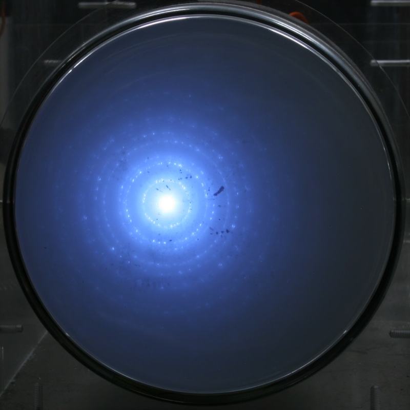 Phosphorescent screen showing bright central spot with concentric blue diffraction rings from electron scattering