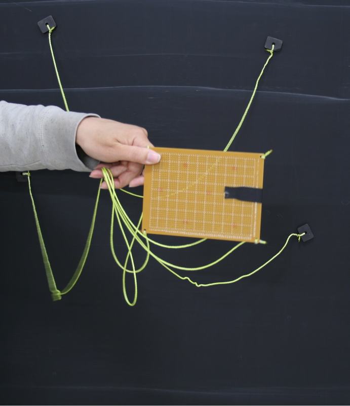 Hand holding orange board at angle with yellow-green strings showing partial disentanglement in progress