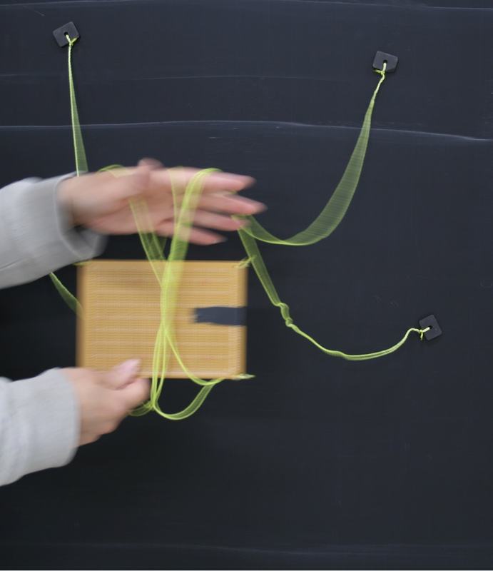 Blurred motion of hands manipulating orange board and yellow-green strings during untangling maneuver