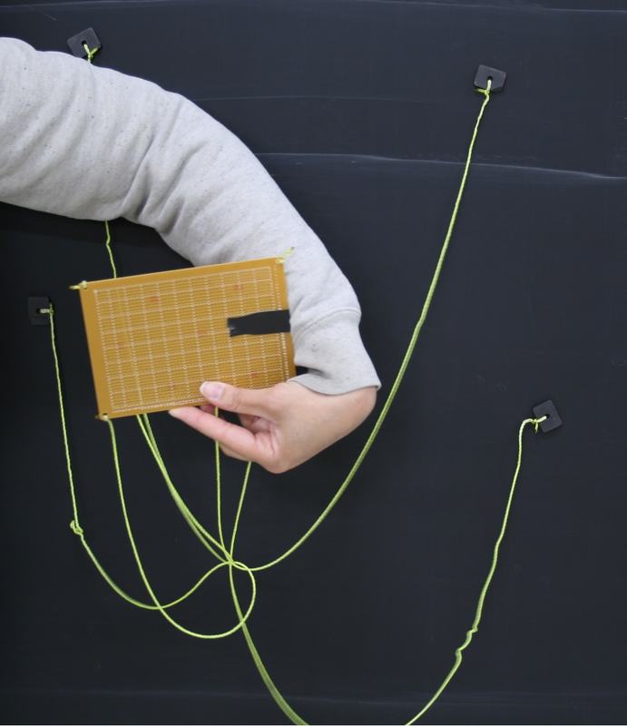 Hand holding orange board with yellow-green strings showing moderate entanglement after partial rotation