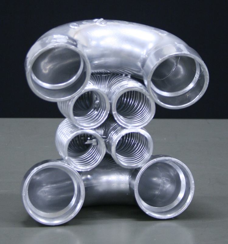 Clear plastic tube structure forming robot-like figure with two large circular eye pieces, four spiral spring sections forming body, and two circular feet