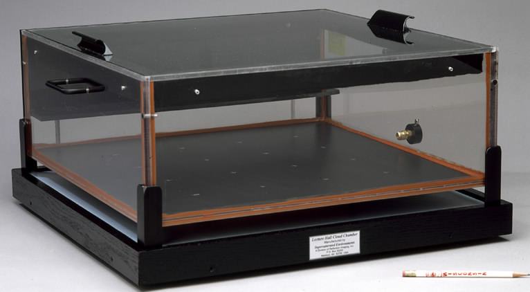 Large rectangular diffusion cloud chamber with glass walls, black base plate, wooden trim, and hinged acrylic lid on a black stand