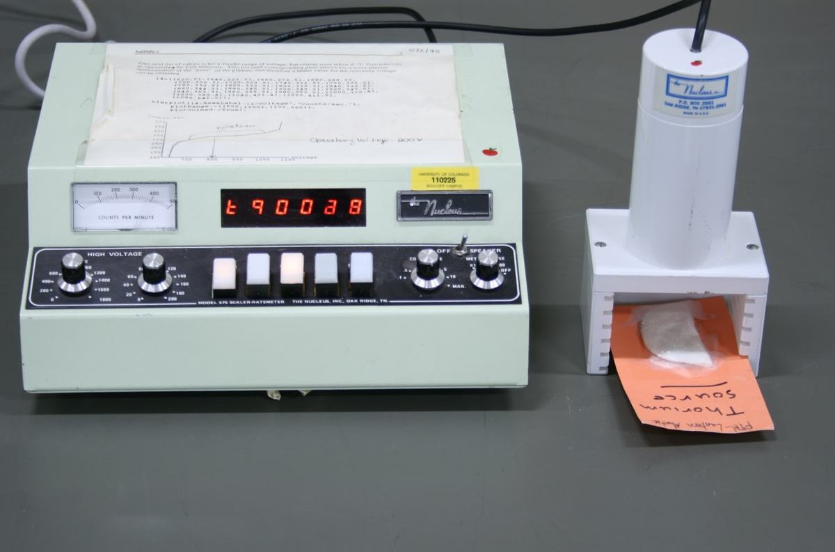 Nucleus Geiger counter displaying 690038 with thorium source card fully positioned on the shelf beneath the detector probe