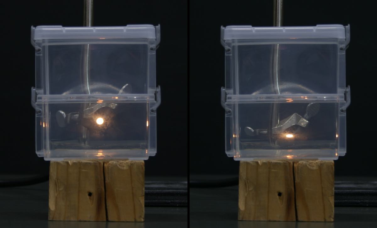 Stereo pair showing two stacked clear plastic containers on wooden blocks, with fiber optic light visible at the boundary between upper and lower containers