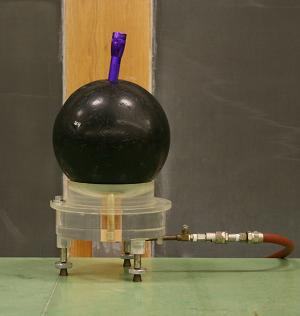 Bowling ball on a transparent air gyroscope base with compressed air hose connected; a Mini Maglite is inserted into a finger hole at the top