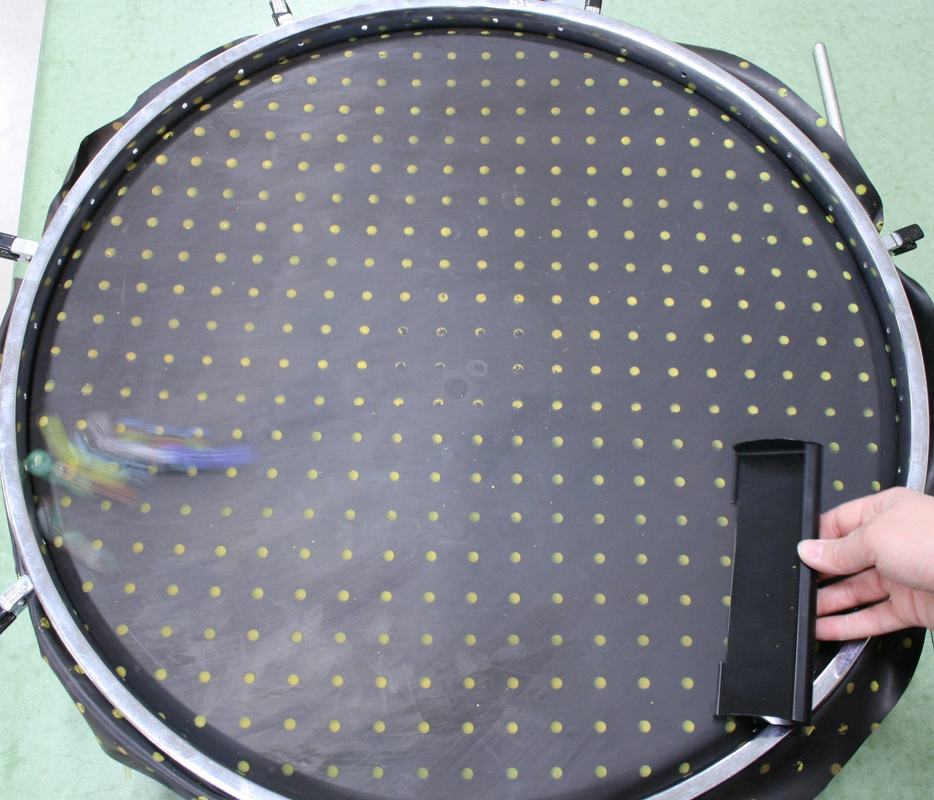 Same apparatus with marbles in motion (blurred) curving across the neoprene sheet, marble launcher held at right edge