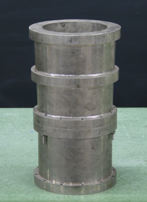 Heavy metal cylindrical X-ray mirror assembly with two main sections joined by flanges, sitting on a green surface